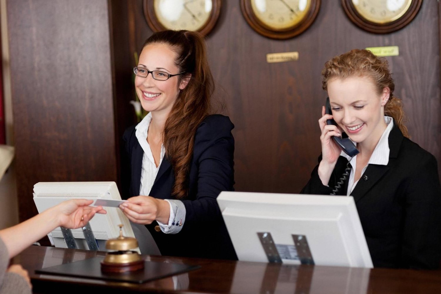 Two hotel receptionists helping guests at the front desk with check-in software